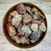 Tumbled stones in various colors including browns, blacks, grays, and vibrant reds showcasing Crazy Lace Agate Tumbled stones that are believed to bring joy and promote optimism.
